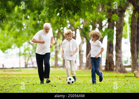 Großvater und Kinder spielen Fußball im sonnigen Park. Glückliche Familie beim Ball. Opa und Kinder spielen Fußball. Die Liebe der Generation. Aktiver Senior-Mann Stockfoto