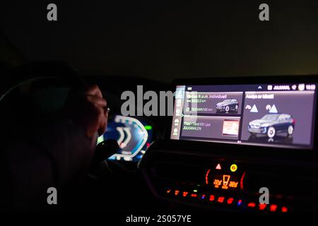 Fahrer, der das BMW iX3 Elektroauto bei Nacht bedient, fokussiert auf beleuchtetes Infotainment-Display und digitales Armaturenbrett mit Details zum Energieverbrauch. Stockfoto