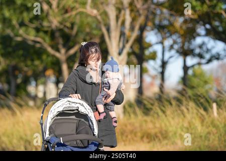 Eine Frau im Alter von 30 Jahren, die mit ihrem 5 Monate alten japanischen Baby einen Kinderwagen schiebt, verbringt einen kalten Winterabend in einem Park in Hakata City. Stockfoto