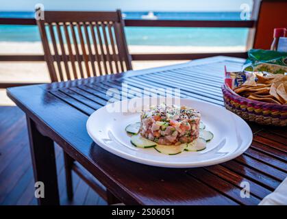 Ein Teller mit frischen Ceviche- und Tortillachips auf einem Holztisch mit Stuhl und Meer im Hintergrund. Stockfoto