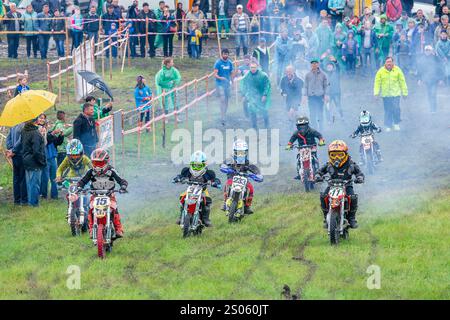 Ukraine, Romny, 2.-3. Juni 2018: Junge Motocross-Fahrer treten auf einer Grasstrecke während der ukrainischen Motocross-Meisterschaft an, umgeben von Zuschauern. Stockfoto