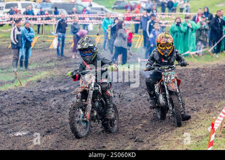 Ukraine, Romny, 2.-3. Juni 2018: Junge Motocross-Fahrer treten auf einer Grasstrecke während der ukrainischen Motocross-Meisterschaft an, umgeben von Zuschauern. Stockfoto