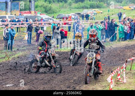 Ukraine, Romny, 2.-3. Juni 2018: Junge Motocross-Fahrer treten auf einer Grasstrecke während der ukrainischen Motocross-Meisterschaft an, umgeben von Zuschauern. Stockfoto