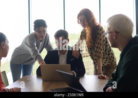 Ein vielseitiges Team von Geschäftsleuten und dem Unternehmensleiter, das geschäftliche Erfolge auf einem Laptop in einem modernen Büro überprüft und diskutiert Stockfoto
