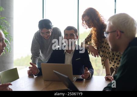 Ein vielseitiges Team von Geschäftsleuten und dem Unternehmensleiter, das geschäftliche Erfolge auf einem Laptop in einem modernen Büro überprüft und diskutiert Stockfoto