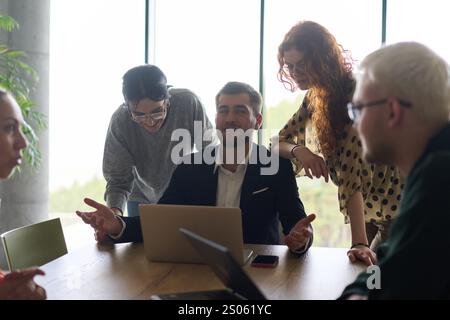 Ein vielseitiges Team von Geschäftsleuten und dem Unternehmensleiter, das geschäftliche Erfolge auf einem Laptop in einem modernen Büro überprüft und diskutiert Stockfoto