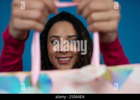 Junge Frau, die eine Geschenktüte mit rosafarbenen Griffen auf blauem Hintergrund zeigt Stockfoto