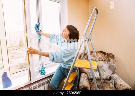 Glückliche Schüchterne, Fröhlich Lächelnde Reife Frau, Die Das Fenster Reinigt. Das Konzept Des Haushalts Und Der Rentner. Kaukasische Frau Im Mittleren Alter. Aktive Senioren Stockfoto
