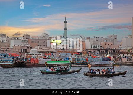 Traditionelle Boote auf dem Bach in Dubai in pulsierender Stadtlandschaft während farbenfroher Sonnenuntergang Stockfoto