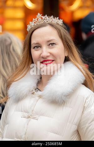 A woman with long hair and a tiara poses in a bustling city decorated with festive decorations and lights creating a festive atmosphere. Stockfoto