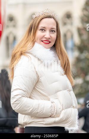 Eine Frau mit langen Haaren, die eine weiße Jacke und eine Krone trägt, steht im Hintergrund der antiken Architektur Österreichs und lächelt. Im Hintergrund ist Stockfoto