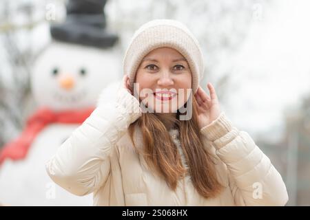 Eine schöne 30-35-jährige Frau steht im Winter vor einem großen Schneemann in einem schneebedeckten Park Stockfoto