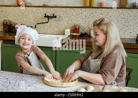 Mutter und Tochter kneten in einer hellen und gemütlichen Küche den Teig zusammen mit einem Lächeln auf dem Gesicht Stockfoto