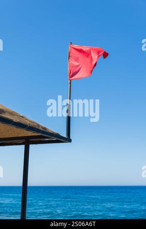 Rote Warnflagge winkt bei starkem Wind unter blauem Himmel am Strand Stockfoto