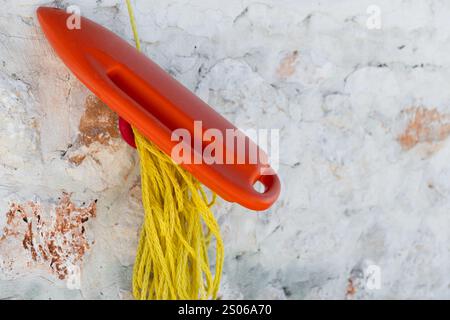 Sicherheitsausrüstung für den Schwimmbereich, rote Rettungskanne mit gelbem Seil an weißer Steinmauer am Strand Stockfoto