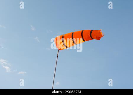 Windsocke. Der rote, gestreifte Windindikator ist an einem sonnigen Tag unter blauem Himmel Stockfoto