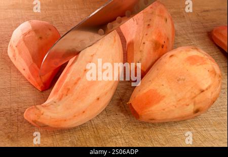 Zerschneiden geschälter Süßkartoffeln auf einem Holzschneidebrett Stockfoto