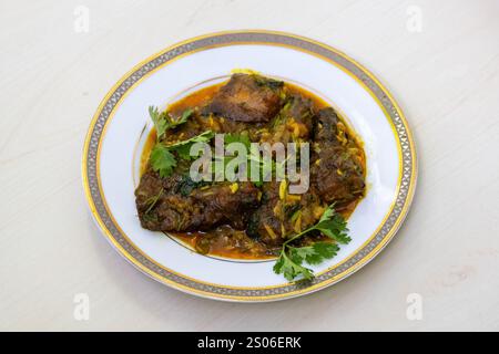 Ein aromatisches Sing Fisch Bhuna Curry, elegant auf einem weißen Teller serviert und mit frischen Korianderblättern geschmückt. Stockfoto