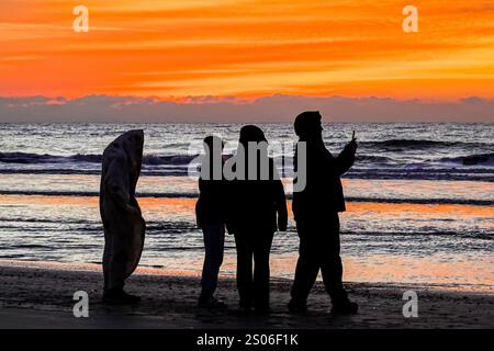 Isle Of Palms, Usa. Dezember 2024. Eine Gruppe junger Menschen, die sich an einem kühlen Weihnachtsmorgen versammelt haben, macht ein Selfie, wenn die Dämmerung über dem Atlantik bricht, am Front Beach, 25. Dezember 2024 in Isle of Palms, South Carolina. Quelle: Richard Ellis/Richard Ellis/Alamy Live News Stockfoto