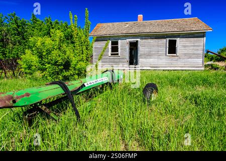 Ein grüner Traktor sitzt auf einem Feld neben einem Haus. Das Haus ist alt und heruntergekommen Stockfoto