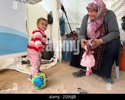 Das palästinensische Kind Yusra Hamaduka, zwei Jahre alt, das einzige Überlebende ihrer Familie, erhält Familienbetreuung von ihrer Großmutter das palästinensische Kind Yusra Hamaduka, zwei Jahre alt, das einzige Überlebende ihrer Familie, erhält Familienbetreuung von ihrer Großmutter und ihren Onkeln in einem Zelt in einem Obdach für Vertriebene in Deir al-Balah im zentralen Gazastreifen am 25. Dezember 2024. Das Kind Yusra überlebte, nachdem das Besatzungsflugzeug in den ersten Tagen des israelischen Krieges im Gazastreifen das Haus ihrer Familie in Gaza-Stadt anvisierte, wo ihr Vater, ihre Mutter und alle drei Geschwister getötet wurden und sie sich in dem Krieg befand Stockfoto