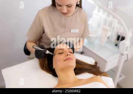 Ein erfahrener Fachmann verwendet ein Mikroneedling-Mesotherapie-Gerät bei einem Patienten in einer ruhigen Klinik, wobei der Schwerpunkt auf Hautverjüngung und Schönheitssteigerung liegt. Die Stockfoto