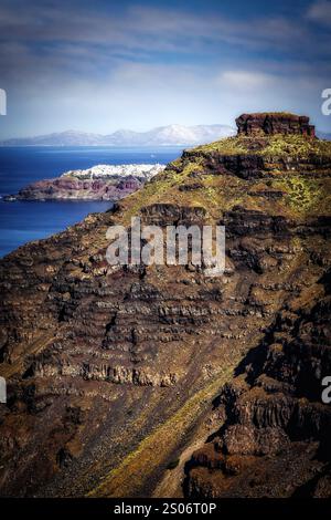 Die dramatischen Klippen des Skaros Rock dominieren den Vordergrund und verbergen teilweise das malerische Dorf Oia am Horizont von Santorini. Stockfoto