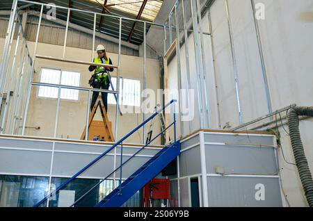 Bauarbeiterin, die Gipskartonplatten auf Metallrahmen mit Wasserwaage und Schraubendreher im Industriebau montiert Stockfoto