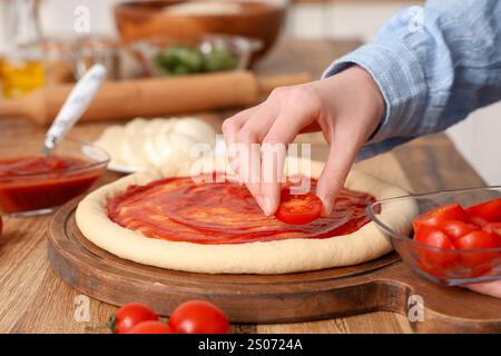 Frau, die Tomaten auf Teig für Pizza in der Nähe des Tisches in der Küche legt Stockfoto