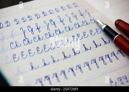 Nahaufnahme von Groß- und Kleinbuchstaben, geschrieben von einem Kind in Kursivschrift mit einem Füllfederhalter mit blauer Tinte in einem gefütterten Notizbuch, einem burgunderroten Brunnen p Stockfoto