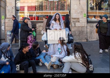 Eine junge israelische Frau in einem Hochzeitskleid hält ein Schild mit der Aufschrift "Ich suche sofort einen Bräutigam für eine Hochzeit". Sie steht am 25. Dezember 2024 in Jerusalem auf der Jaffa Road. Israel Stockfoto