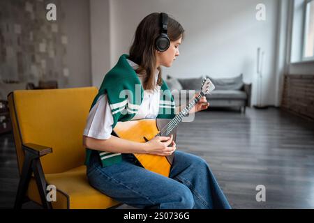 Eine fokussierte Frau spielt Balalaika, fühlt Musik zu Hause über Kopfhörer, übt das Zupfen von Saiten Stockfoto