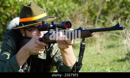 Hunter in Tarnung zielt sein Gewehr in einen dichten Wald und verschmilzt mit der natürlichen Umgebung. Das Bild zeigt eine Verbindung zwischen Mensch und Natur. Stockfoto