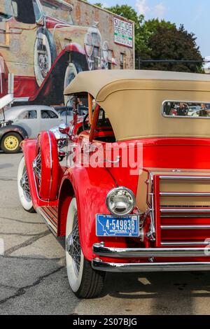 Ein orangefarbener Duesenberg Phaeton auf einer Autoausstellung entlang der West Ninth Street gegenüber einem Wandbild eines ähnlichen Autos in Auburn, Indiana, USA. Stockfoto