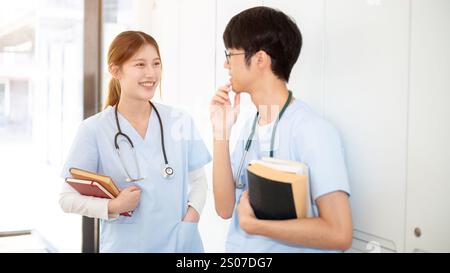Zwei glückliche asiatische Ärztinnen oder Medizinstudenten tragen ihre Lehrbücher, während sie in der Umkleidekabine stehen und reden. Medizinstudium Stockfoto