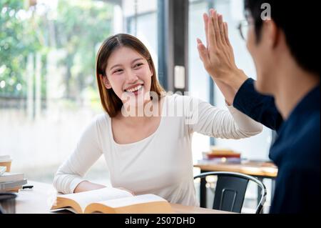 Zwei fröhliche junge asiatische College-Studenten geben sich gegenseitig fünf, um ihren Examenserfolg zu feiern, während sie gemeinsam in einer Bibliothek oder Co studieren Stockfoto