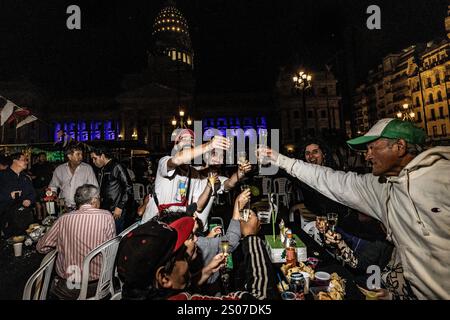 Buenos Aires, Argentinien. Dezember 2024. Die Mitglieder eines der Tische am Heiligabend stoßen um Mitternacht an. Das Weihnachtsessen vor dem Nationalkongress wurde von der Gruppe Argentina Humana and the Movement of Excluded Workers (MTE) organisiert, die aus Hunderten von Menschen besteht, die ihren Lebensunterhalt durch das Recycling von Müll verdienen. Der Slogan lautete „keine Familie ohne Weihnachten“. Quelle: SOPA Images Limited/Alamy Live News Stockfoto