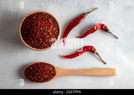 Rote Chiliflocken. Rote Chiliflocken in einer Holzschale auf grauer Oberfläche. Getrocknete Chiliflocken. Stockfoto