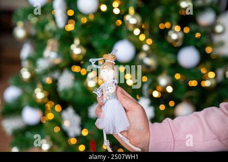 Eine Person hält eine kleine weiße Puppe vor einem Weihnachtsbaum. Die Puppe trägt ein weißes Kleid und hat ein Diadem auf dem Kopf. Stockfoto