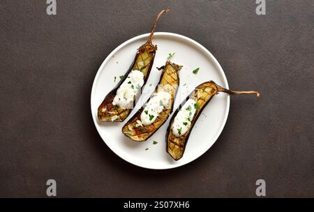 Gebackene Aubergine mit Knoblauch-Joghurt-Dressing auf Teller über dunklem Hintergrund mit Kopierraum. Draufsicht, flach Stockfoto