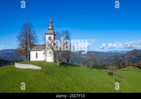 Malerischer Blick auf die Kirche saint Tomaz auf einem grünen Hügel in slowenien, umgeben von herbstlicher Natur und einer Bergkette am Horizont. St. tomas Stockfoto