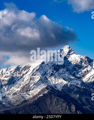 Ein atemberaubender Blick auf schneebedeckte Berge unter einem blauen Himmel mit flauschigen Wolken. Die Gipfel sind zerklüftet und majestätisch und zeigen die Schönheit der Natur. Stockfoto
