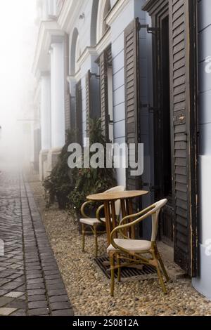 Eine ruhige Morgenszene mit einem hölzernen Café-Tisch und Stühlen vor dem Hintergrund einer nebeligen Straße Stockfoto