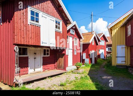 An einem sonnigen Sommertag Reihen sich alte rot bemalte Holzhäuser entlang einer grasbewachsenen Gasse im historischen Zentrum von Smögen, Schweden. Stockfoto