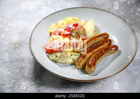Kartoffelsalat mit kleinen gebratenen Würstchen, ein beliebtes schnelles Gericht für Partys und Feiertage wie Weihnachten und Neujahr, graue Platte auf Steinoberfläche, Stockfoto