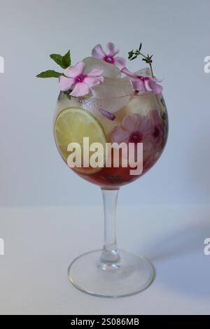 Weinglas gefüllt mit Eis, rosa Blumen, Limette und rotem Getränk Stockfoto