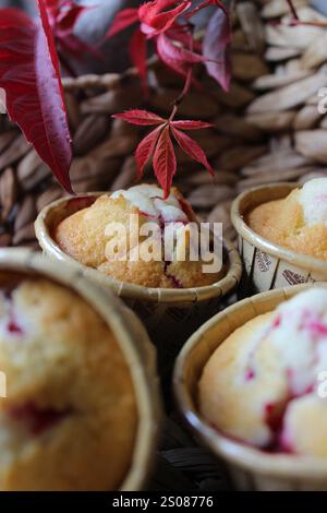 Frisch gebackene Cranberry-Muffins kühlen auf einem Korbblech, verziert mit lebhaften Herbstblättern, schaffen eine gemütliche und einladende Szene Stockfoto