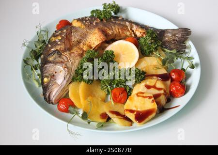 Gegrillter Wolfsbarsch serviert mit gebratenen Kartoffeln, Kirschtomaten, frischer Petersilie und einer Scheibe Zitrone, was eine gesunde und geschmackvolle Mahlzeit schafft Stockfoto