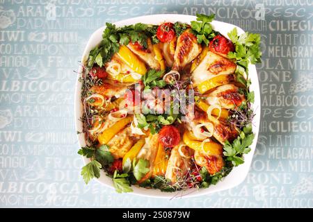 Aromatisch gebratene Hähnchenschenkel in einer Auflaufform mit bunten Paprika, Zwiebeln, Tomaten, Knoblauch, Petersilie, und Thymian, der Appetit erzeugt Stockfoto