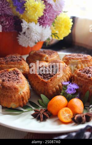 Köstliche Muffins in Herzform mit Schokolade und Kumquat sind wunderschön mit Blumen und Sternanis auf einem weißen Teller dekoriert Stockfoto